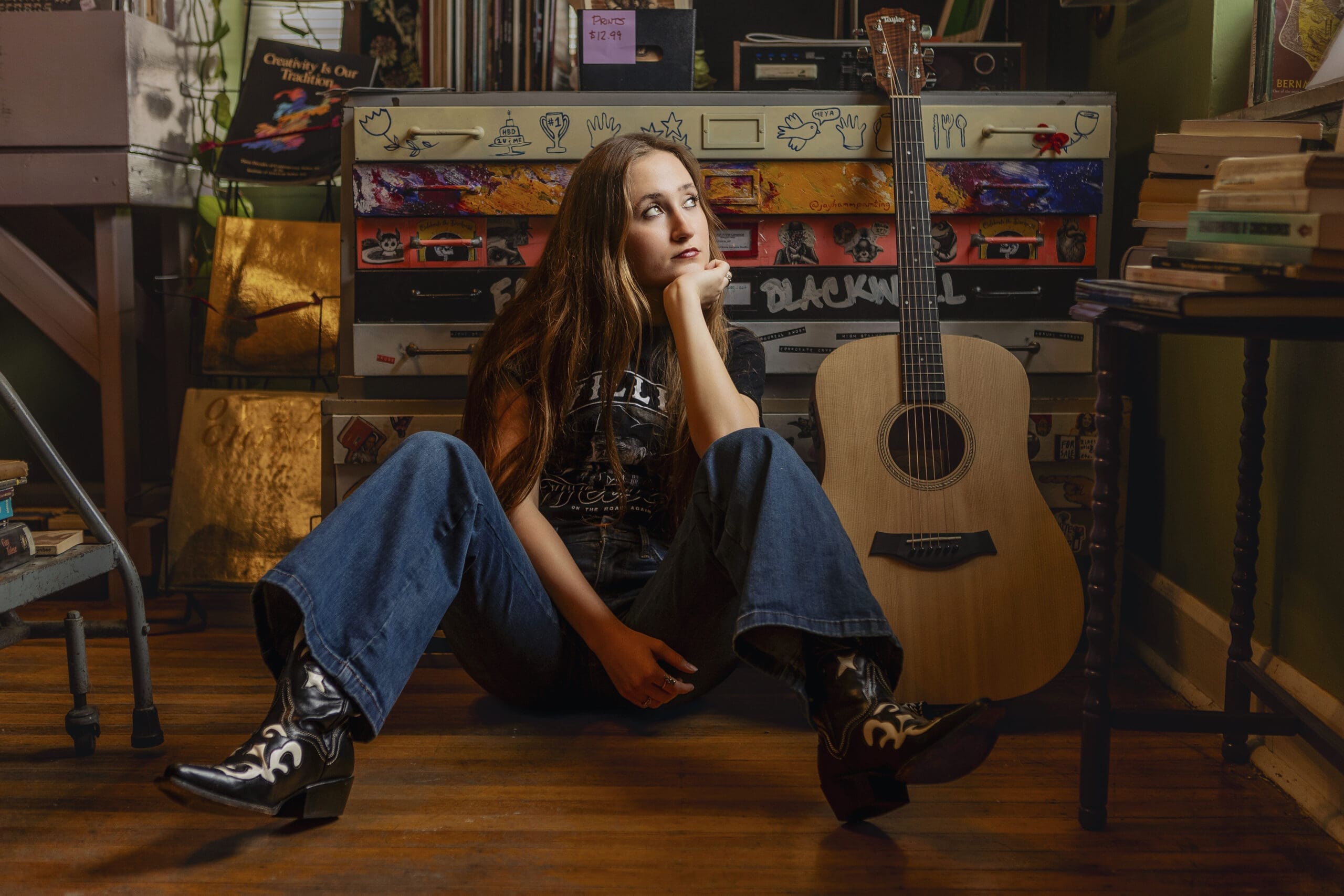 High school senior girl reading a book in a library during her senior picture session, surrounded by bookshelves and warm natural tones.