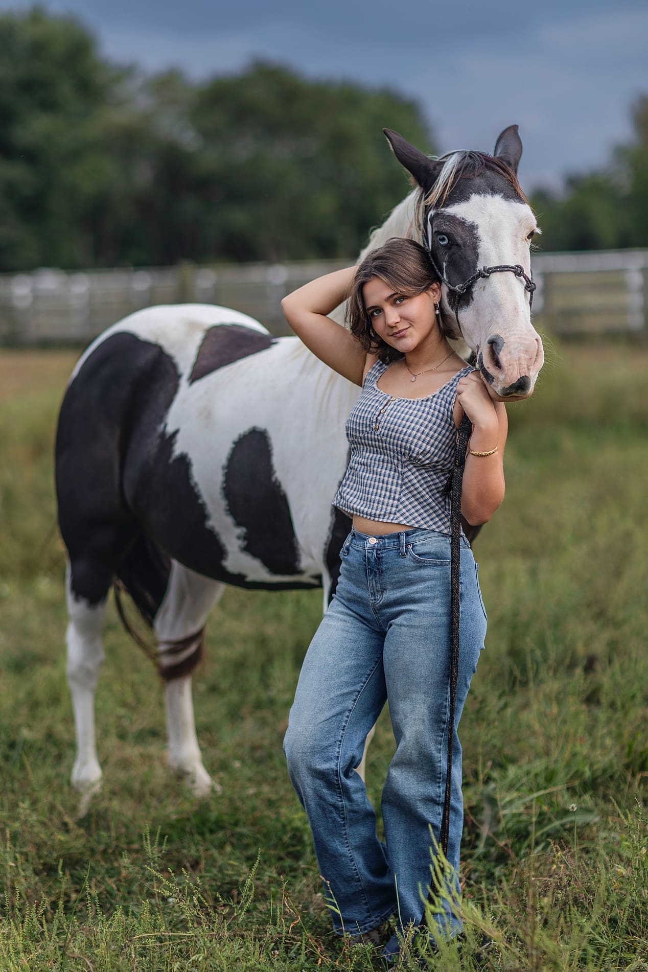 SENIPR MODEL OF THE YEAR High school senior girl posing with her black and white paint horse in a grassy field during an outdoor senior picture session in Indiana.